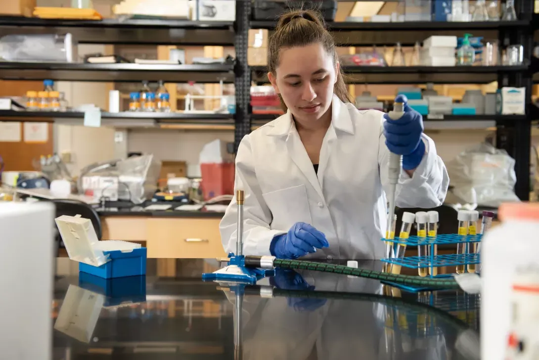 Student in biology lab using a pipette to transfer chemicals